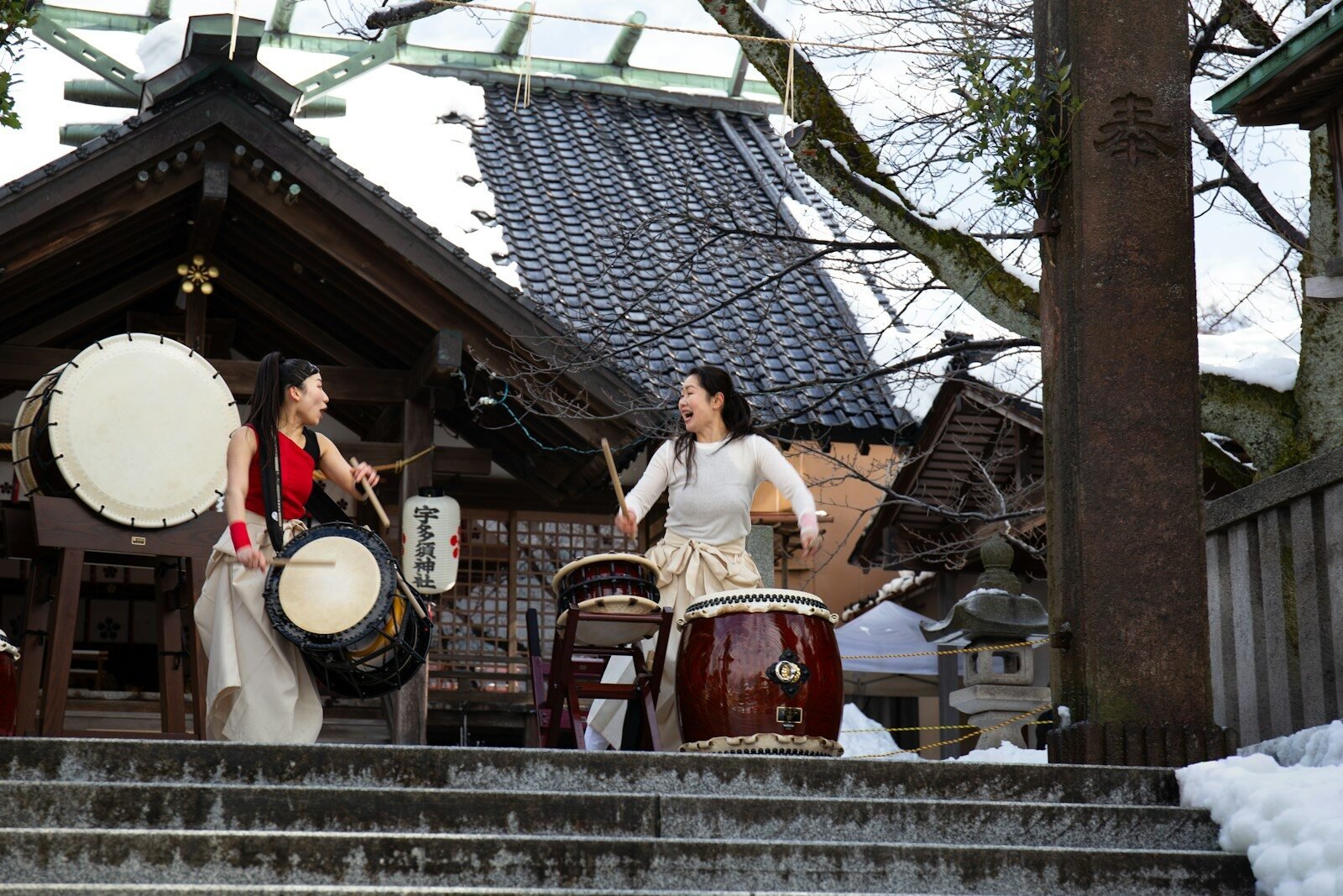 Two women playing drums in front of a temple